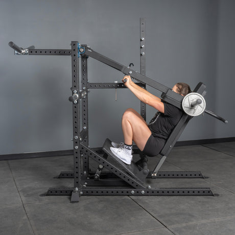 A person uses the Bells of Steel Pandemonium Squat – 3-in-1 Pendulum Squat / Calf Press / Viking Press Machine, sitting with their back on padded support and feet on the slanted platform, gripping handles while performing a squat in the gym.