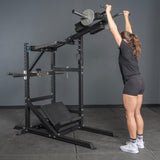 Someone in athletic wear grips the handles of the Bells of Steel Pandemonium Squat – a 3-in-1 Pendulum Squat, Calf Press, and Viking Press Machine. Its sturdy black frame and attached weights make it ideal for any home gym.