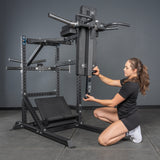 A woman in athletic wear adjusts the vertical pad of the Bells of Steel Pandemonium Squat – a 3-in-1 Pendulum Squat / Calf Press / Viking Press Machine, with sturdy metal supports and foot platforms, ideal for any home gym or intense workout.