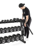 A person in black attire and a cap organizes hex dumbbells on the Bells of Steel Residential Dumbbell Rack, featuring multiple rows with various weights for a perfect home gym setup. The plain white background highlights the sleek organization of this equipment.