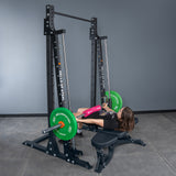 A person performs a hip thrust on a Bells of Steel Smith Machine - Hydra (3" x 3", ⅝" Holes), supporting a barbell with green plates and a pink pad across their hips in a modern gym.