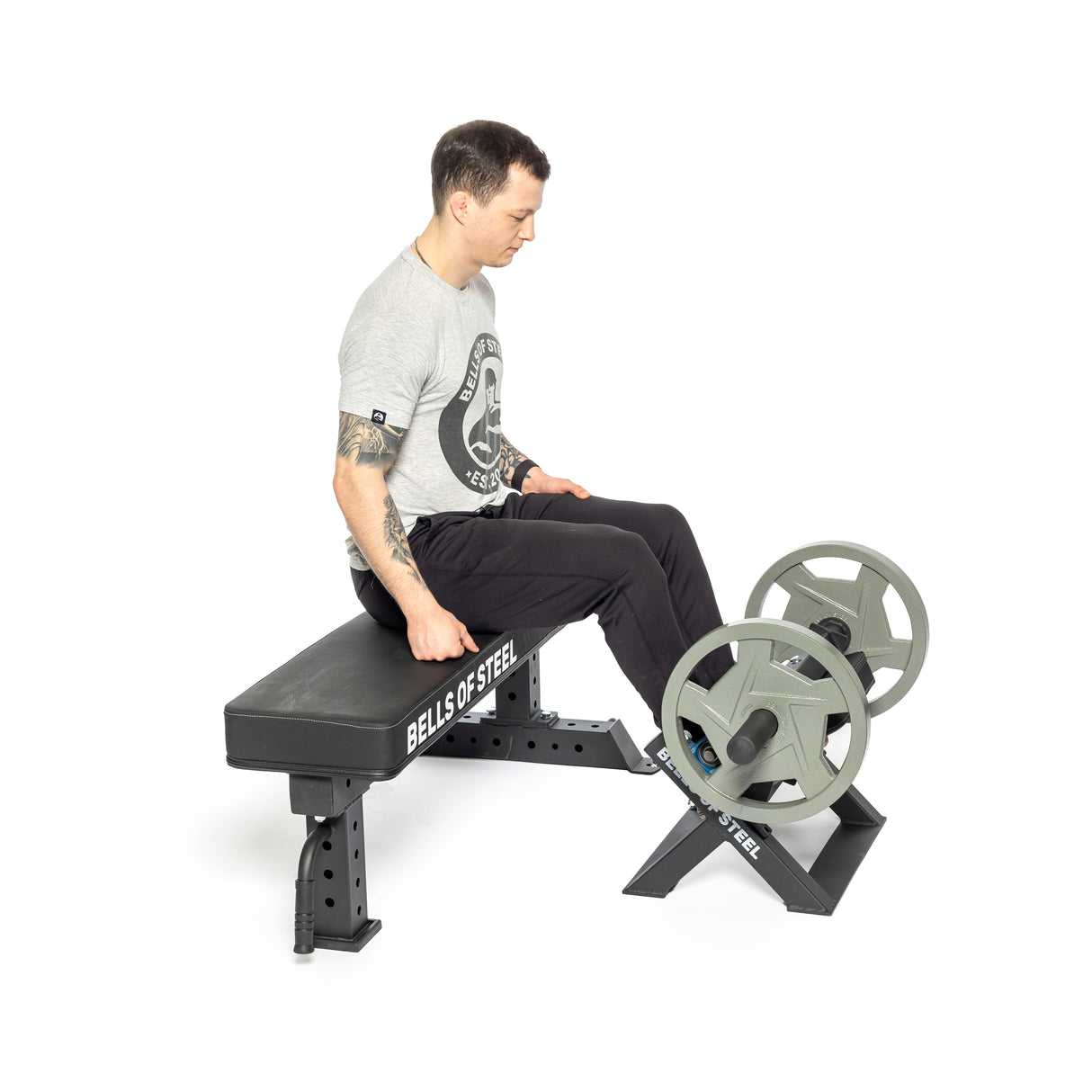 A person on the Tibialis Trainer Machine from Bells of Steel focuses on hypertrophy by pressing weighted steel plates. Wearing a gray T-shirt and black pants, they engage in strength training exercises with precision.