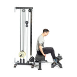 A person seated on a bench is performing a calf raise using the Tibialis Trainer Machine by Bells of Steel, lifting a chain-weighted barbell with their feet while maintaining a straight back. This workout employs tall machinery with pulleys and weights for optimal hypertrophy.