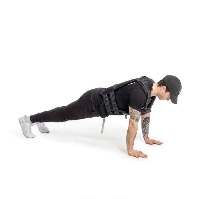 Clad in a black cap and outfit, an individual demonstrates a push-up on a white background using the Bells of Steel Canada Weighted Vest and Plates. The vest securely holds steel plates as they extend their arms fully with feet together, showcasing impeccable form.